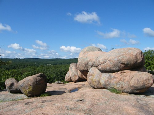 Large, smooth boulders on a rocky surface with a blue sky and green hills in the background.