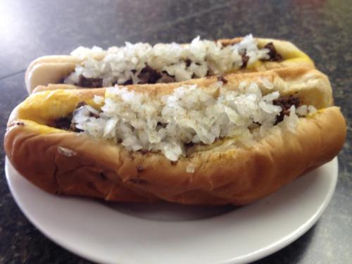 Two hot dogs in buns topped with chopped onions, served on a white plate.