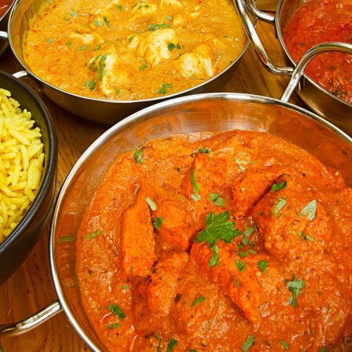 A vibrant spread of Indian dishes, including chicken curry, lentil soup, and yellow rice, garnished with herbs.