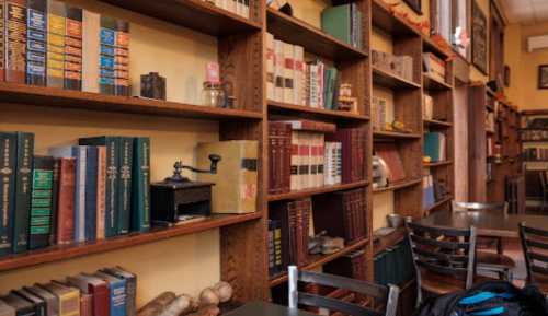 A cozy café interior featuring wooden bookshelves filled with colorful books and vintage items, with tables and chairs.