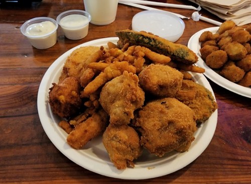 A plate of assorted fried foods, including chicken, okra, and fries, with two small cups of dipping sauce.