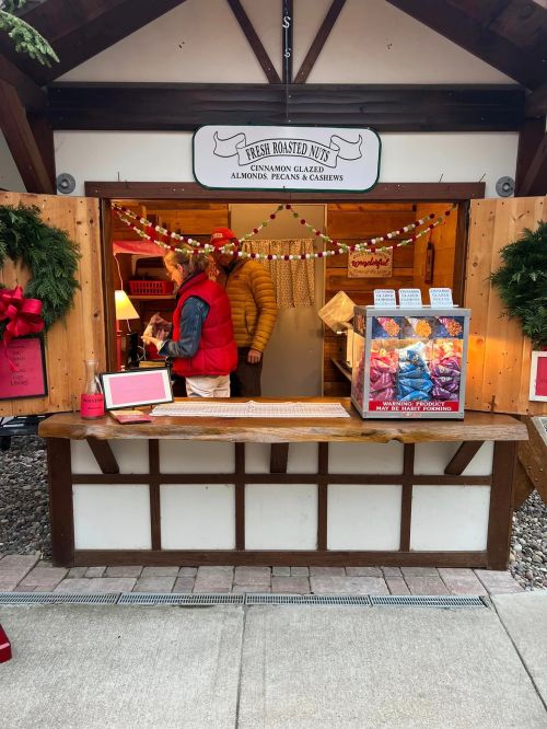 A festive market stall selling fresh roasted nuts, decorated with holiday garlands and a sign above.