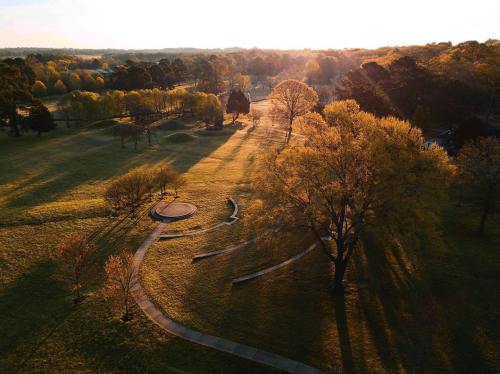 Aerial view of a park at sunset, featuring trees, pathways, and long shadows across the grassy landscape.
