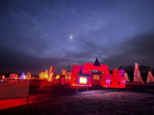 A colorful display of holiday lights featuring a castle and trees against a twilight sky.