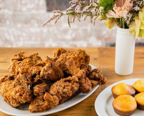 A platter of crispy fried chicken next to a vase of flowers and a plate of cornbread muffins on a wooden table.