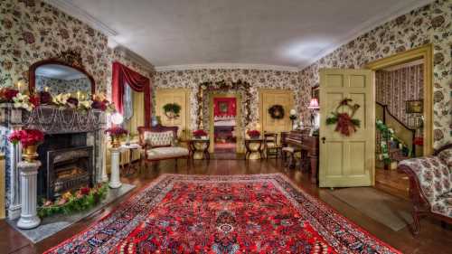 Cozy living room decorated for the holidays, featuring a fireplace, floral wallpaper, and a vibrant red area rug.