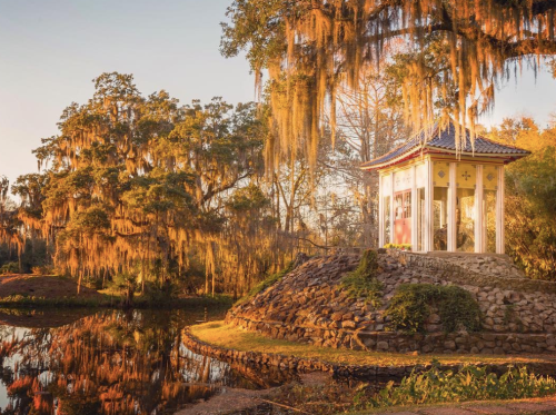 A serene gazebo by a calm pond, surrounded by trees draped in Spanish moss, illuminated by warm sunset light.