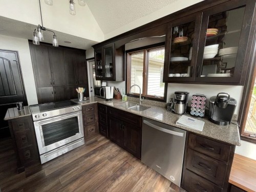 Modern kitchen with dark wood cabinets, stainless steel appliances, and a granite countertop, featuring a window view.