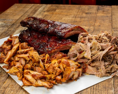 A platter of barbecue featuring ribs and pulled pork, served on a wooden table.