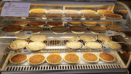 A display case filled with various pies, including apple, peach, cherry, and pecan, labeled "Lea's Pies."