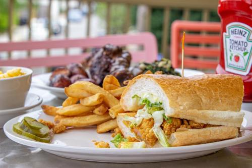 A plate featuring a fried chicken sandwich with lettuce, fries, pickles, and a side of macaroni and cheese. Ketchup in the background.