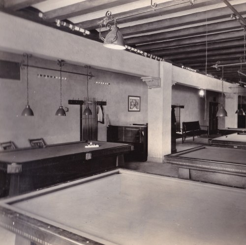 A vintage billiard room with two pool tables, pendant lights, and wooden beams on the ceiling.