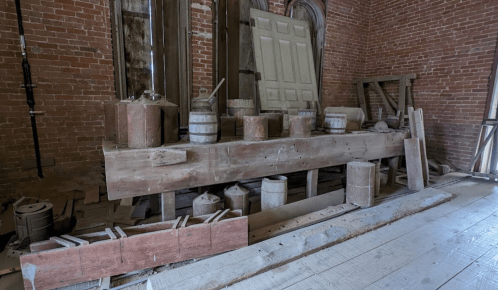 A rustic interior with wooden barrels, planks, and a door leaning against a brick wall, creating a vintage atmosphere.