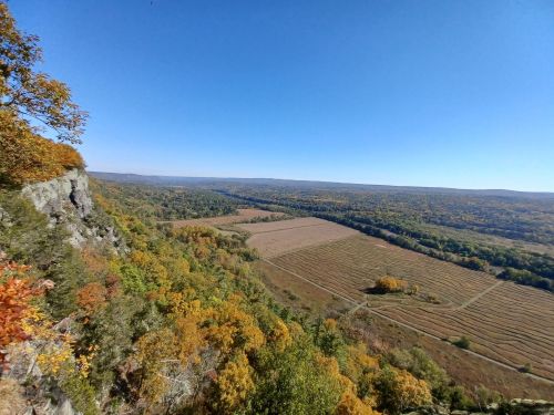 A panoramic view of a valley with autumn foliage, featuring rolling hills and clear blue skies.