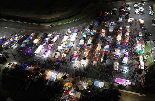 Aerial view of a vibrant night market with colorful tents and crowds, illuminated by various lights.
