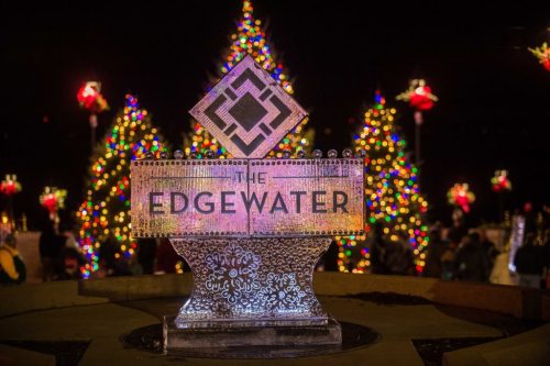 Illuminated sign for The Edgewater surrounded by colorful holiday trees and festive decorations at night.