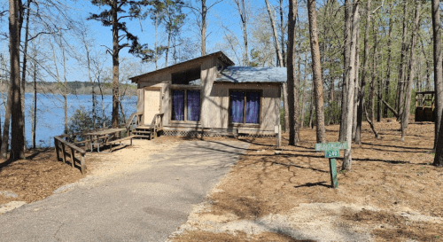 A cabin by a lake surrounded by trees, with a sign indicating "Bungalow 248" and a gravel path leading to it.