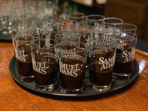 A tray of Samuel Adams glasses filled with dark beer, arranged neatly on a wooden table.