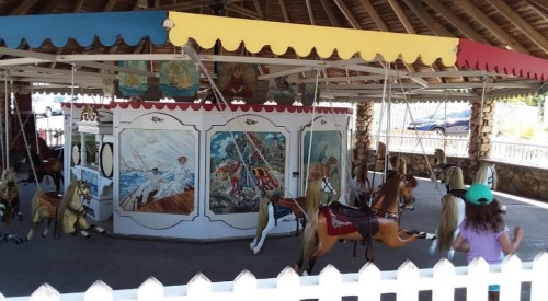 A vintage carousel with painted horses and colorful canopies, surrounded by a white picket fence.