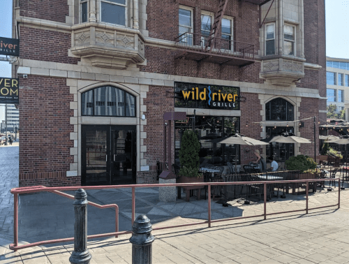 Exterior of Wild River Grille, a brick building with outdoor seating and large windows, on a sunny day.