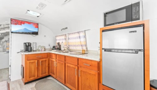 A modern kitchen in an Airstream trailer featuring wooden cabinets, a microwave, and a stainless steel refrigerator.