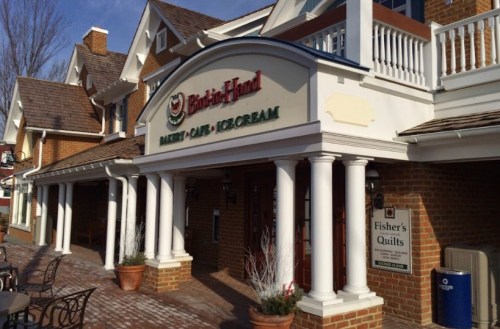Exterior of a bakery and ice cream shop with a sign, featuring brick walls and white columns.