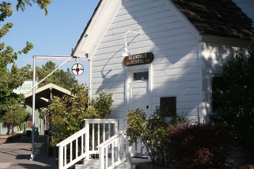 A white building with a sign reading "Glendale School" and a small porch, surrounded by greenery.