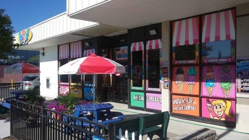 Colorful ice cream shop exterior with striped awnings, outdoor seating, and vibrant window displays of ice cream flavors.