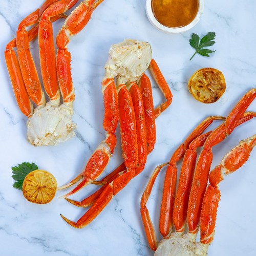 Three cooked crabs with bright orange shells, accompanied by a small bowl of sauce and garnished with lemon and parsley.