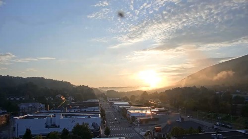Sunrise over a small town, with mist rising from the hills and soft clouds in the sky, illuminating the street below.