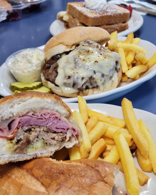 A plate with a cheeseburger, fries, coleslaw, and a sandwich with ham, alongside a dessert of waffles.