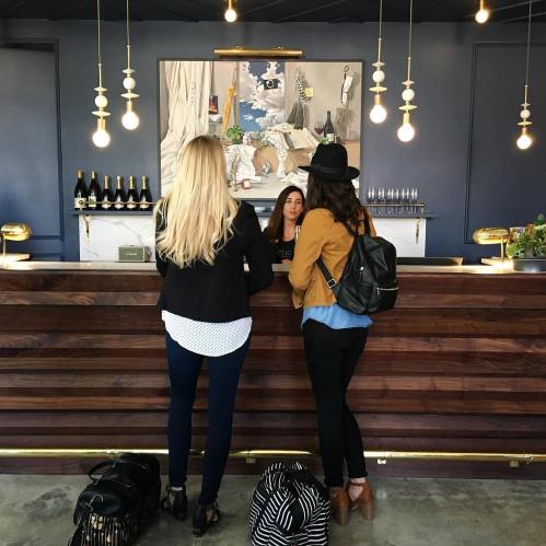 Two women at a modern reception desk, with a stylish art piece and pendant lights in the background.