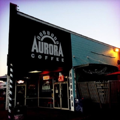 Exterior of Aurora Coffee shop, featuring a sign and warm lighting in the evening.