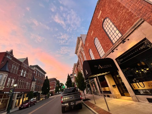 A street view at sunset featuring brick buildings, a restaurant called "the Alcove," and a parked truck.