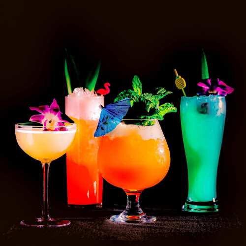 Four colorful cocktails with garnishes, including flowers and umbrellas, set against a dark background.