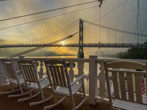 A serene view of a bridge at sunrise, with rocking chairs in the foreground and mist over the water.