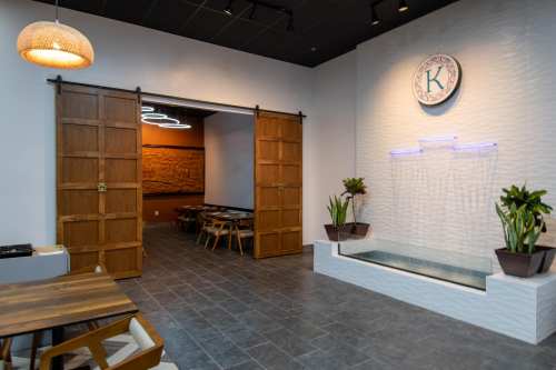 Interior of a modern restaurant featuring wooden doors, a water feature, and decorative plants.