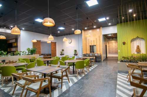 Modern restaurant interior with green chairs, wooden tables, and decorative lighting, featuring plants and a cozy atmosphere.