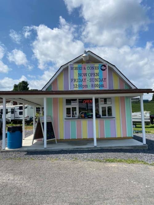 Colorful ice cream stand with a sign reading "Bones & Cones" open Friday to Sunday, 12:00 PM to 8:00 PM.
