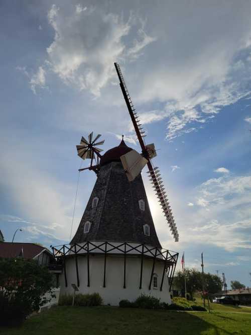 A tall windmill with a red roof and large blades, set against a blue sky with scattered clouds.