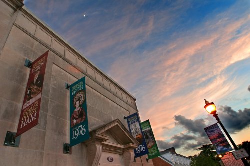 A building with colorful banners and a sunset sky, featuring clouds and a hint of the moon.