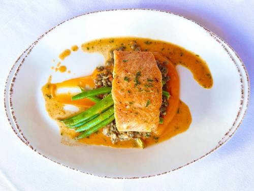 A plated dish featuring salmon on a bed of lentils, garnished with green beans and a flavorful sauce.