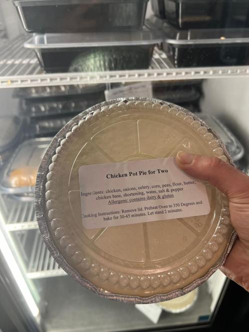 A hand holding a chicken pot pie labeled "Chicken Pot Pie for Two" with ingredients and cooking instructions visible.
