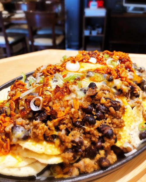 A close-up of a sizzling plate of nachos topped with ground meat, black beans, cheese, and green onions.