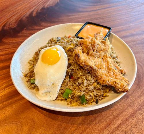 A plate of fried rice topped with a sunny-side-up egg, fried chicken, and a small container of sauce.