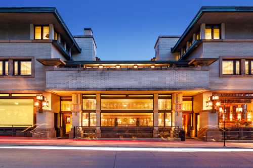 A historic building with a modern design, featuring large windows and warm lighting, set against a twilight sky.