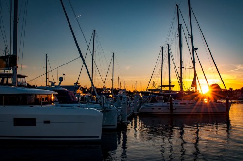 Sailboats docked in a marina at sunset, with vibrant colors reflecting on the water.