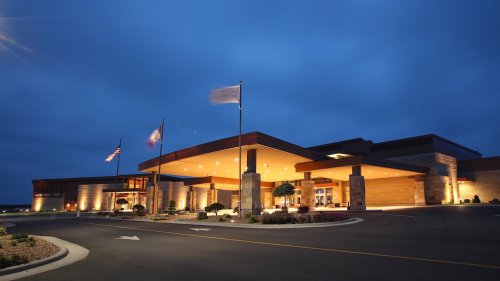 A modern building at dusk, featuring a welcoming entrance and flags, surrounded by landscaped grounds.