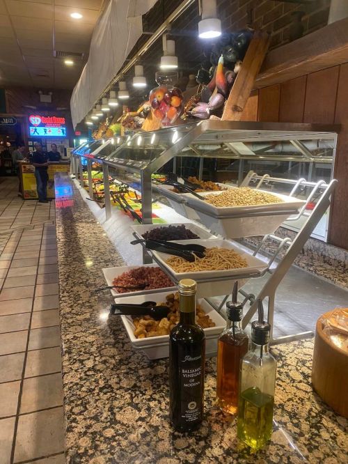 A buffet with various dishes, including pasta, salads, and oils, set on a granite countertop in a restaurant.