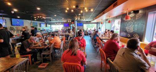 A busy restaurant interior with patrons dining at tables, watching screens, and enjoying a lively atmosphere.